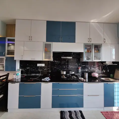 U-shaped kitchen with teal-blue and white high-gloss shutters, a black marble-look backsplash, chimney hood over the gas hob and glass-front display cabinets