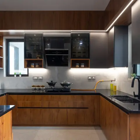 U-shaped kitchen with wood-grain lower cabinets, dark grey glass-front upper units, a black granite countertop, and profile lighting along the ceiling edge.