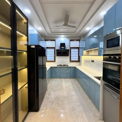 U-shaped modular kitchen in high-gloss teal acrylic with white quartz counters, twin grilled windows flanking a black chimney