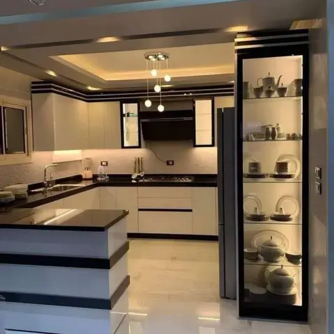 U-shaped modular kitchen with glossy white and black cabinetry, a black granite island counter, a tiered cove-lit ceiling with cluster pendant lights