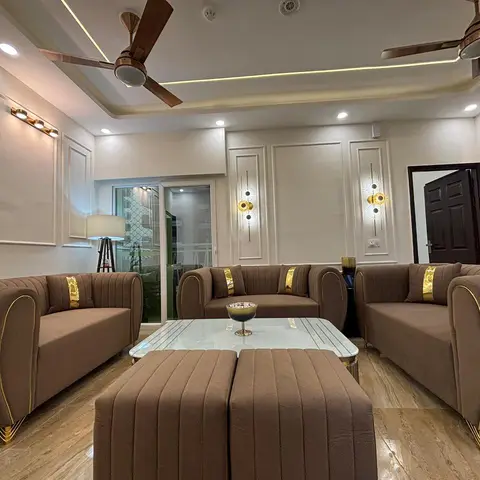 U-shaped seating of channel-tufted mocha velvet sofas with gold trim legs around a glass-and-brass coffee table and matching ottomans