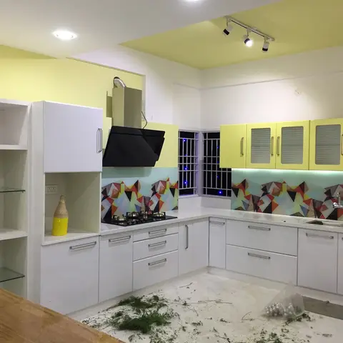 U-shaped white glossy kitchen with pale yellow upper cabinets, a colorful geometric mosaic backsplash, a black chimney hood