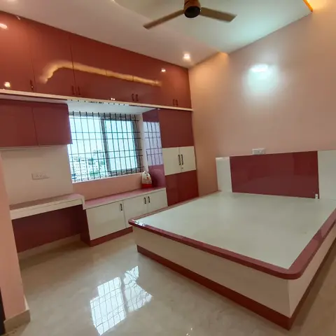 Under-construction bedroom with a glossy maroon-and-white built-in bed platform, matching wardrobe, and a window-side study counter.