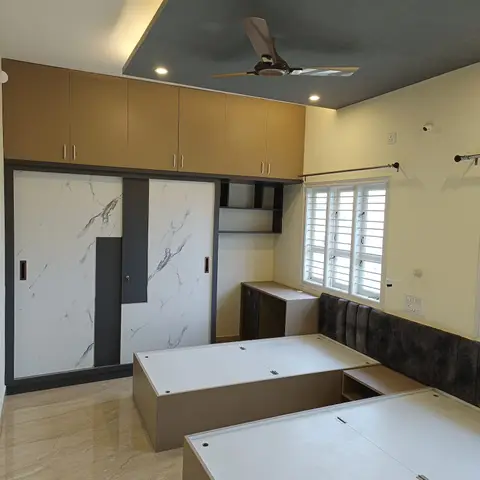 Under-construction bedroom with two side-by-side built-in storage bed platforms, a marble-finish sliding wardrobe, and an angular grey cove-lit false ceiling.