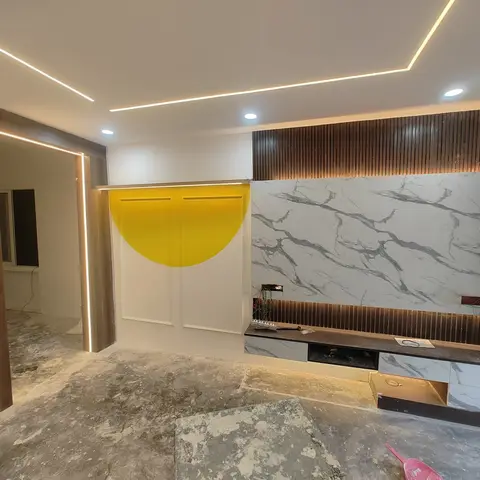 Under-construction living room TV feature wall with a bookmatched marble-veined panel and fluted wood surround above a floating marble-top console