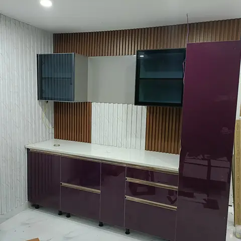 Under-construction living room TV wall in glossy wine-purple joinery against fluted wood and marble-effect wallpaper panelling