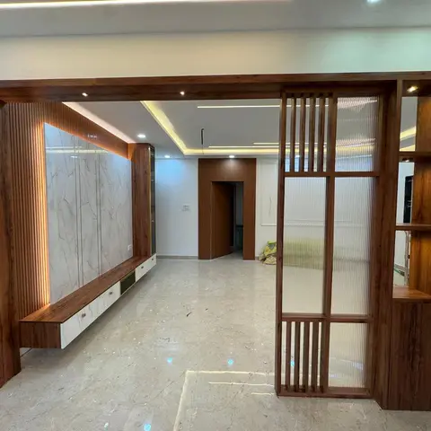 Under-construction living room with a floating wood-and-marble TV console flanked by fluted panelling and a timber-slat jaali partition screen