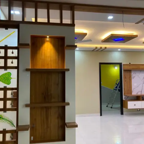 Under-construction pooja partition in teak with stepped shelves and a spot-lit niche, its side panel set with painted flute