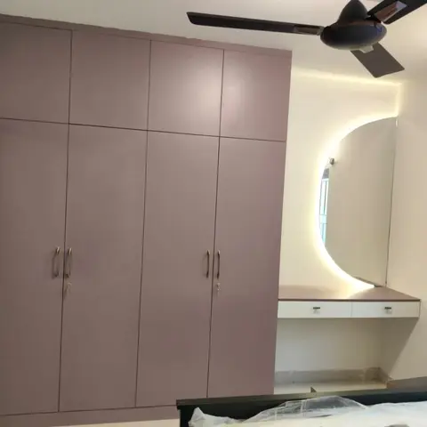 Under-finishing master bedroom with a mauve laminate wardrobe and a backlit asymmetric dressing mirror on a built-in console