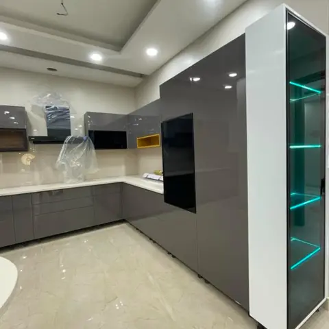 Under-installation grey gloss L-shaped kitchen still wrapped in protective plastic, with a tall glass display unit lit by green LED shelves