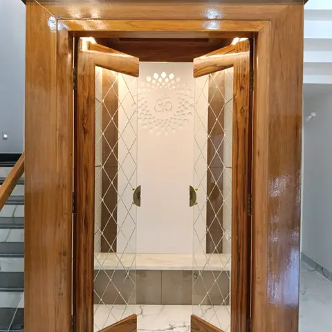 Under-stair pooja unit with glossy teak wood diamond-glass doors opening to a backlit lotus-and-Om wall motif above a marble altar shelf.
