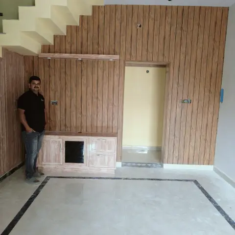 Under-stair TV wall in an empty new-build hall clad in vertical wood-grain laminate with a low matching console, wiring still hanging loose
