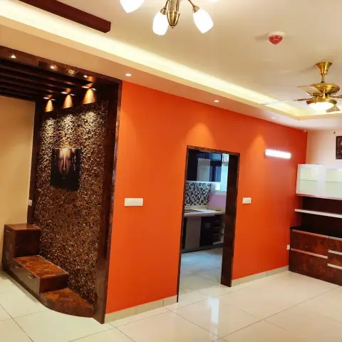 Unfurnished dining hall painted bright orange, with a brown pebble-mosaic feature wall carrying a Buddha panel over a stepped platform