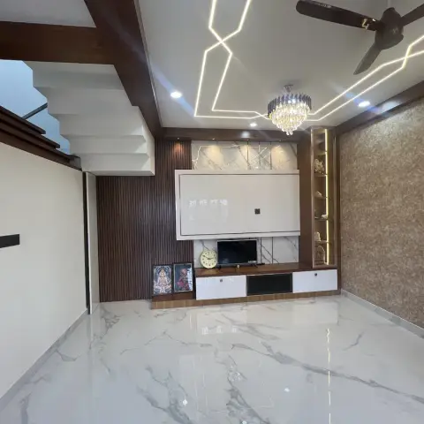 Unfurnished duplex hall with a fluted-walnut and marble TV wall, backlit display niches holding brass idols, a zig-zag linear LED pattern in the false ceiling