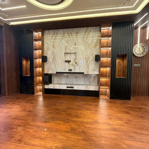 Unfurnished living room with a marble-look TV feature wall flanked by backlit fluted wood display niches and a circular cove-lit AC ceiling detail