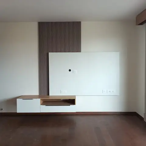 Unstyled living room with a floating walnut-and-white TV console against a fluted wood panelling backdrop