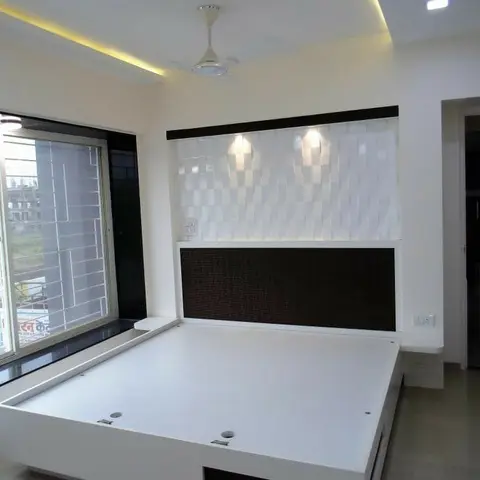 Unstyled white platform storage bed with a 3D textured white wall panel headboard and cove-lit ceiling, no bedding yet.