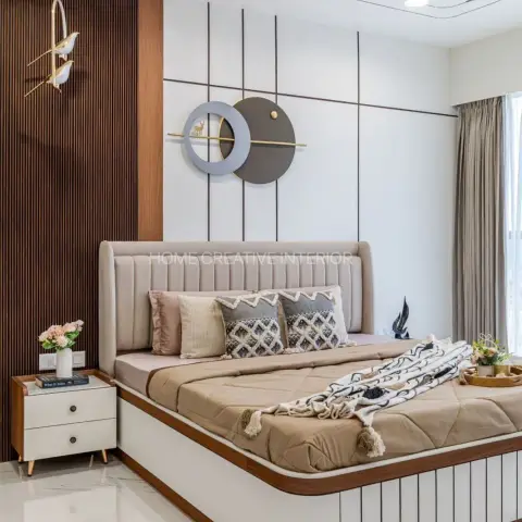 Upholstered channel-tufted bed against a fluted wood accent wall with a round metallic wall sculpture and a bird-motif pendant light beside it.