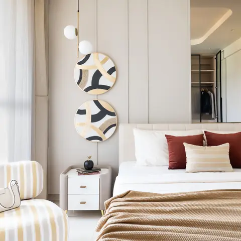 Upholstered-panel bedroom wall with two round gold-and-black wall discs beside a bed, with an open walk-in wardrobe visible in the mirror behind.
