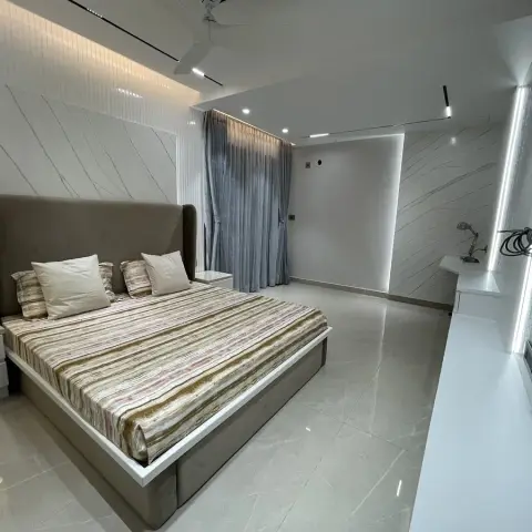 Upholstered wing-back bed on a white plinth against marble-veined wall slabs, with a narrow fluted panel band