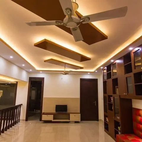Upper-floor family lounge with a floating cove-lit ceiling, a low wood TV console, and a tall glass-front storage unit beside a red tufted bench.