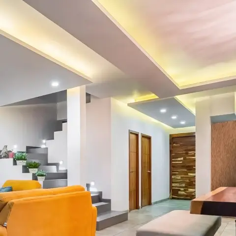 Upward-tilted view of a double-height living area: mustard velvet sofas below stepped grey display shelves tucked under an open staircase