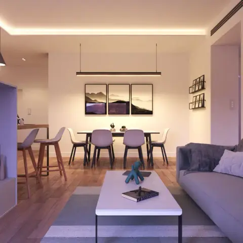 V-Ray render of an open-plan living-dining lit only by warm ceiling cove, with a grey sofa facing a wall-hung TV on a handleless white unit and a triptych of