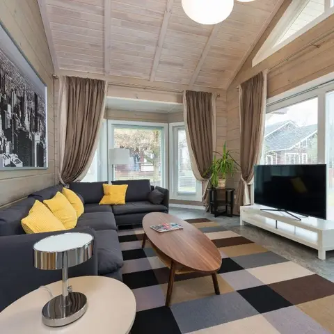 Vaulted wood-plank living room with a charcoal sectional sofa, mustard accent pillows and a black-and-white checkered rug