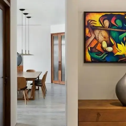 View from a gallery-wall passage, past a wood console with ceramic vases, into a dining area with a wood table, chairs, and a cluster of pendant lights.
