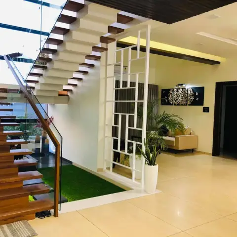 Villa entry hall with a cantilevered teak-tread staircase behind a glass balustrade, a pocket of artificial turf under the flight