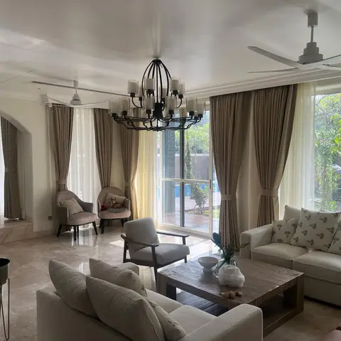 Villa living room with floor-to-ceiling glass doors opening to a pool and garden, a wrought-iron candle chandelier