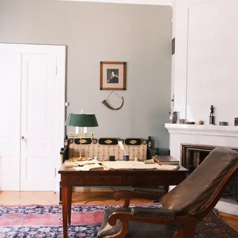 Vintage study corner with an antique writing desk, green banker's lamp, leather wingback chair and a marble fireplace mantel.