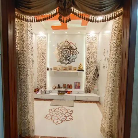 Walk-in pooja room with a gold laser-cut mandala above a backlit white niche, jaali side panels, a tasselled swag valance across the walnut-framed opening