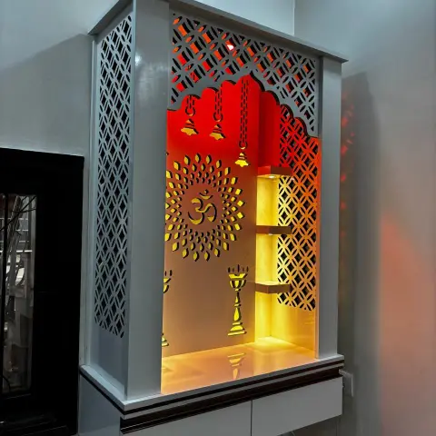 Wall-hung white pooja mandir with CNC-cut jaali side panels and a scalloped arch, an Om-and-diya cutout backboard washed red into amber
