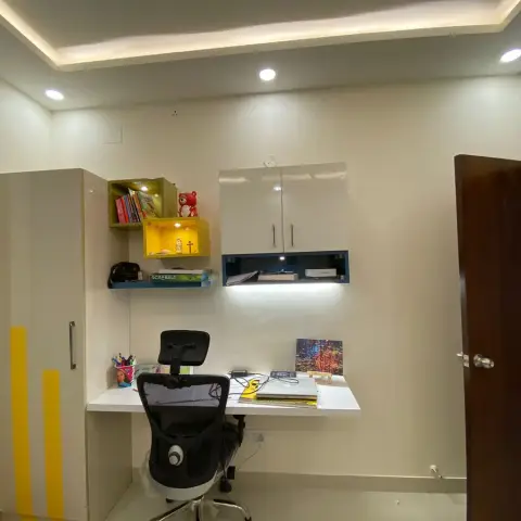 Wall-hung white study desk under a closed overhead unit and an open blue-lined niche, with green and yellow display cubes holding children's books and a teddy