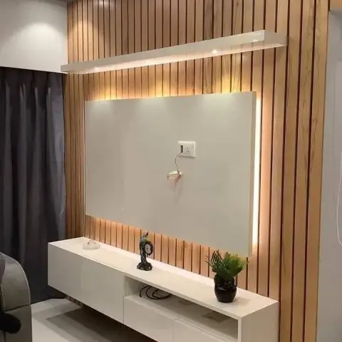 Wall-hung white TV console under a backlit off-white panel set into a full-height teak slat wall