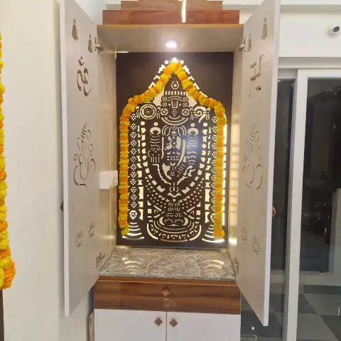 Wall-mounted pooja mandir with CNC-cut Om and Ganesha shutters opened onto a backlit Balaji panel