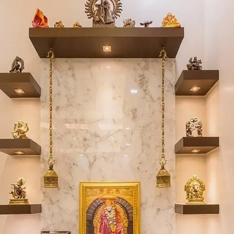Wall-mounted pooja shrine with a book-matched marble backing panel, a golden deity frame, hanging brass bells