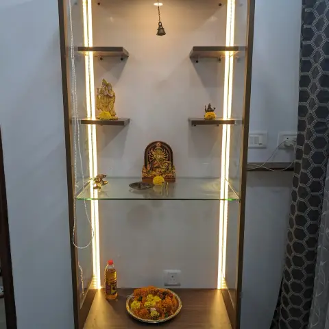Wall-mounted pooja unit in walnut laminate with a scalloped temple-arch pelmet, warm LED strips down both inner reveals