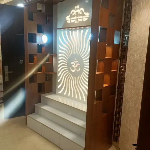 Wall-mounted pooja unit with a backlit sunburst Om panel, cubby-hole wooden joinery frame, and a white marble step plinth at the entrance foyer.