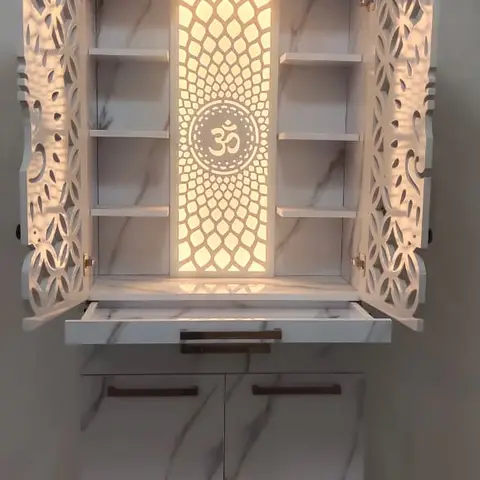 Wall-mounted white marble-finish pooja unit with a backlit carved Om jaali panel and jali-cut cabinet doors, storage below.