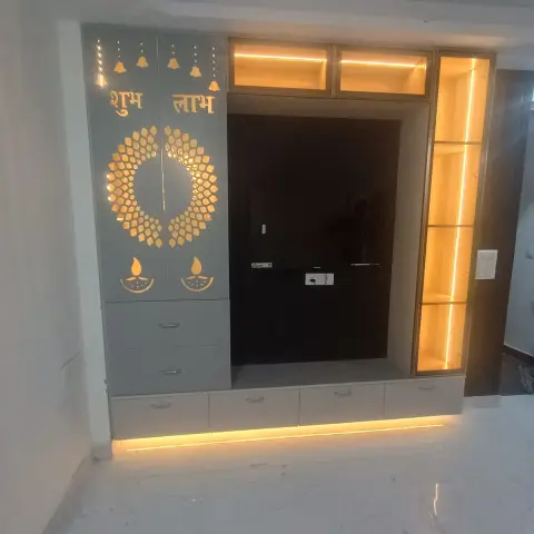 Wall-set pooja unit with grey CNC-cut shutters reading Shubh Labh above a backlit gold marigold ring and two diya motifs