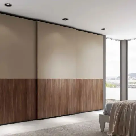 Wall-to-wall sliding wardrobe in a bedroom, shutters split horizontally into beige matt lacquer above and walnut veneer below, running up to a corner window.
