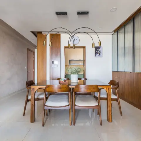 Walnut dining table with a dark glass top and six curved-back chairs, lit by twin brass arc pendants