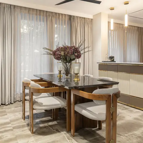 Walnut-framed dark-marble dining table for six with curved boucle armchairs, backed by full-height sheer and pinch-pleat linen drapes