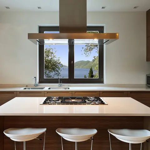 Walnut-veneer kitchen wrapped around a central island with a five-burner hob and a bronze-trim island hood