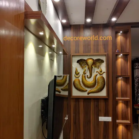 Walnut veneer TV feature wall with an exposed wood-beam ceiling, an open lit display niche, and a brass Ganesh wall art panel.