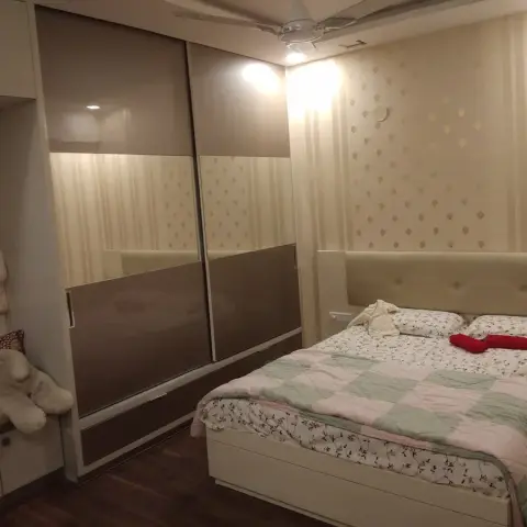 Warm-lit bedroom with a beige tufted headboard against striped gold-motif wallpaper, a two-tone mirrored sliding wardrobe opposite