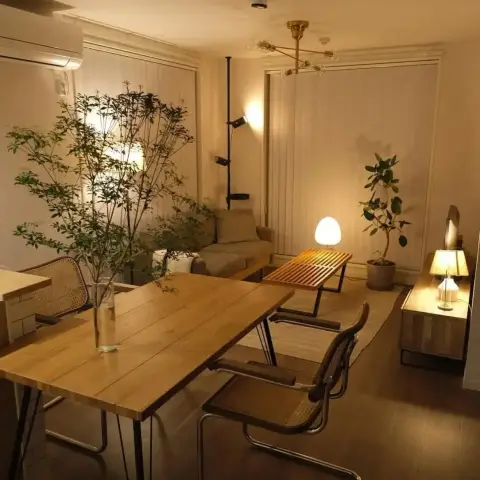 Warmly lit open dining-living space with a wood dining table and cane Cesca chairs beneath a brass sputnik pendant, a low wood-slat coffee table