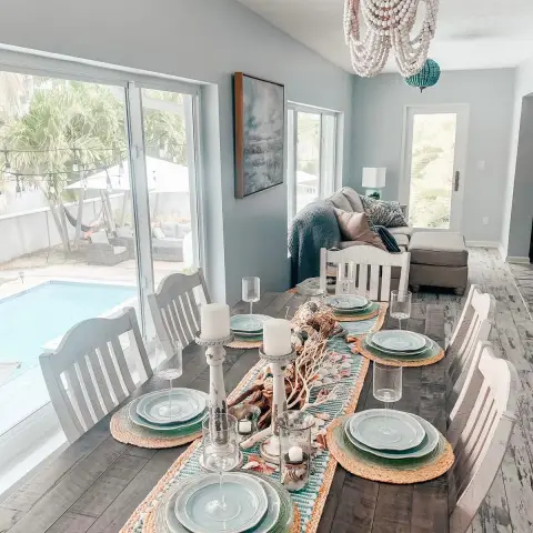 Weathered plank dining table laid with sea-green glass chargers on jute mats and a driftwood-and-shell runner
